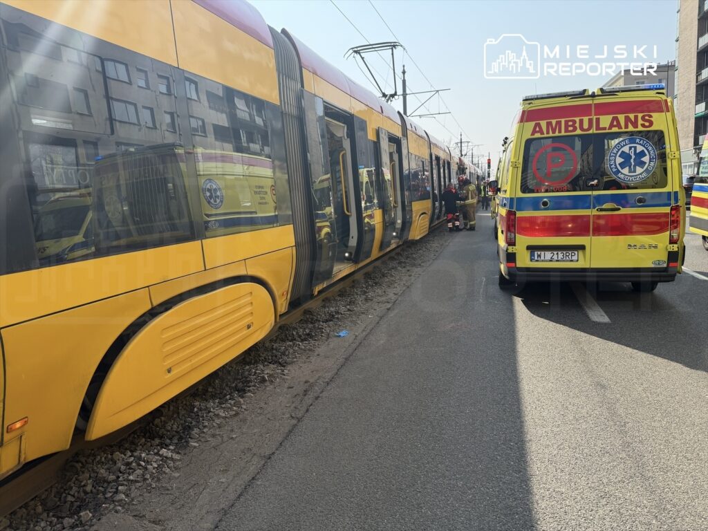 Żółty tramwaj zatrzymany przy torowisku, obok stoi karetka pogotowia oraz zespół ratunkowy w akcji.