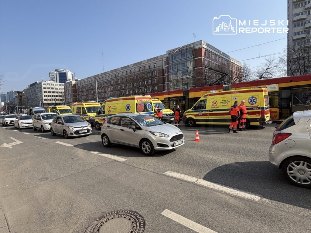 Karetki pogotowia z ratownikami na ulicy, obok zatoru drogowego w miejskim otoczeniu.