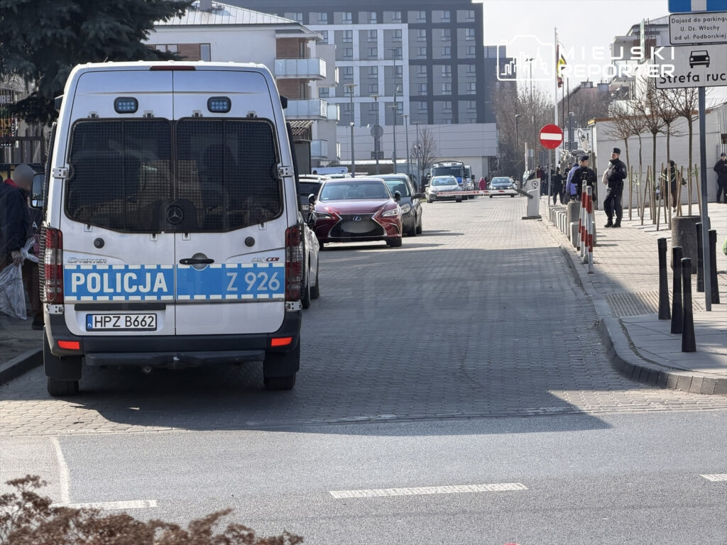 Radiowóz policyjny zaparkowany na ulicy, obok stojący funkcjonariusze w mundurach.