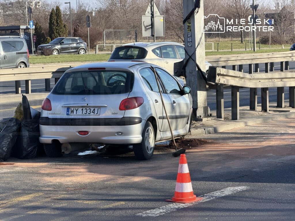 Samochód osobowy zaparkowany nieprawidłowo przy krawężniku, obok leżą worki na śmieci i pachołek drogowy.