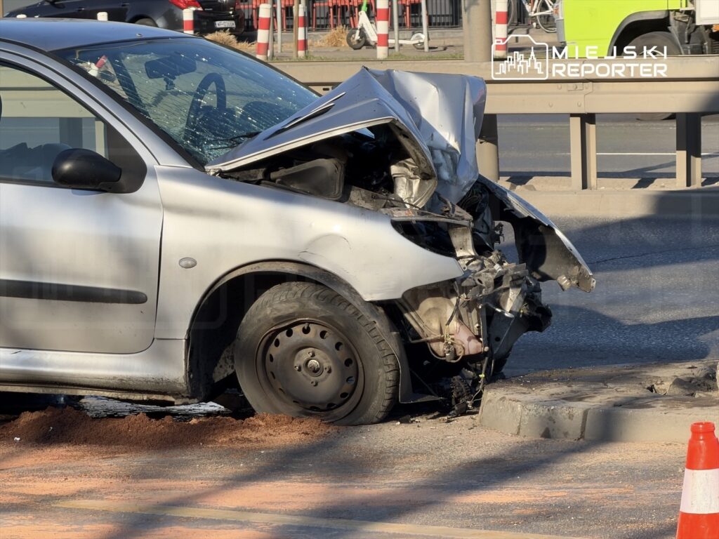 Uszkodzony samochód osobowy z wgniecioną przednią częścią stoi na drodze obok krawężnika.