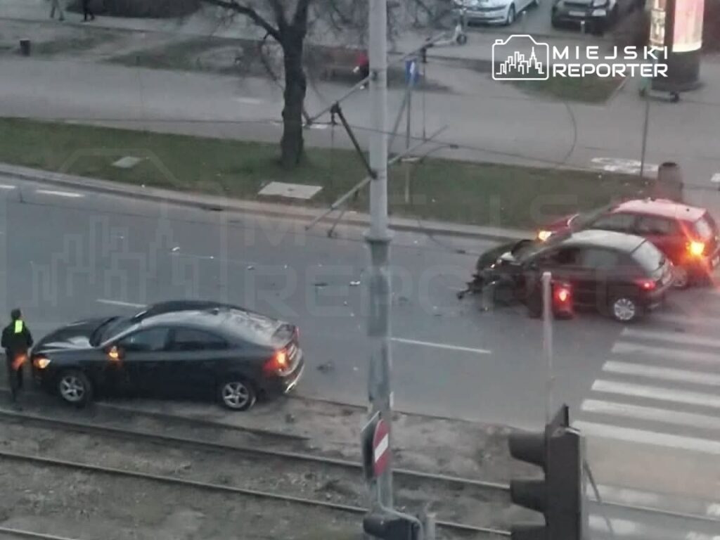 Dwa uszkodzone samochody osobowe po kolizji na ulicy, obok policjant zbierający informacje.