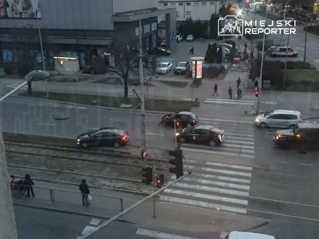 Ruch uliczny w godzinach wieczornych, samochody zatrzymane na skrzyżowaniu, piesi przechodzą przez pasy.