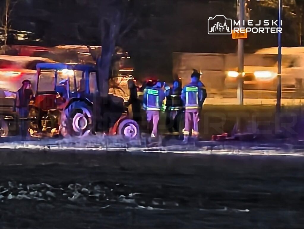 Grupa ratowników w odzieży ochronnej pracuje przy przewróconym ciągniku w ciemnej scenerii nocnej.