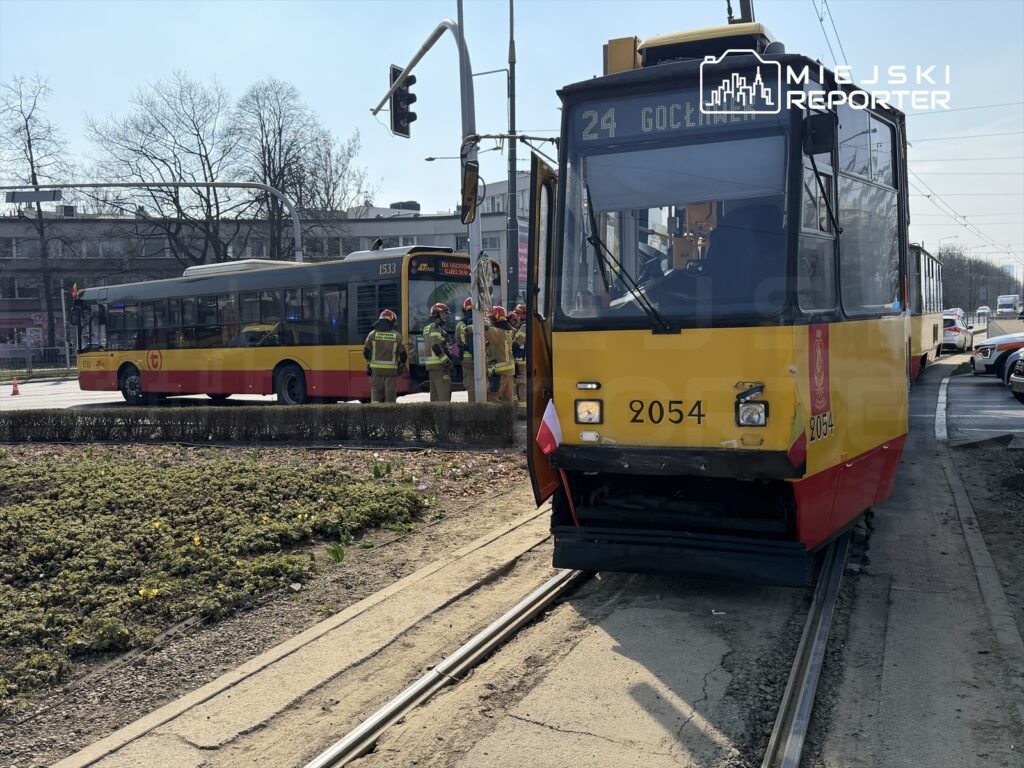 Tramwaj z numerem 2054 stoi na torach, obok grupy ratowników w mundurach, w pobliżu ruchliwej ulicy.