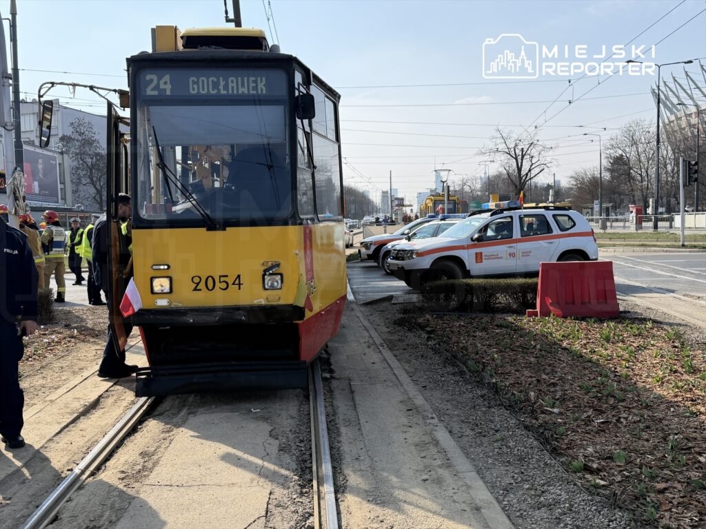Tramwaj linii 24 zatrzymany na torowisku, obok policyjne i ratunkowe pojazdy, w tle nowoczesne budynki.