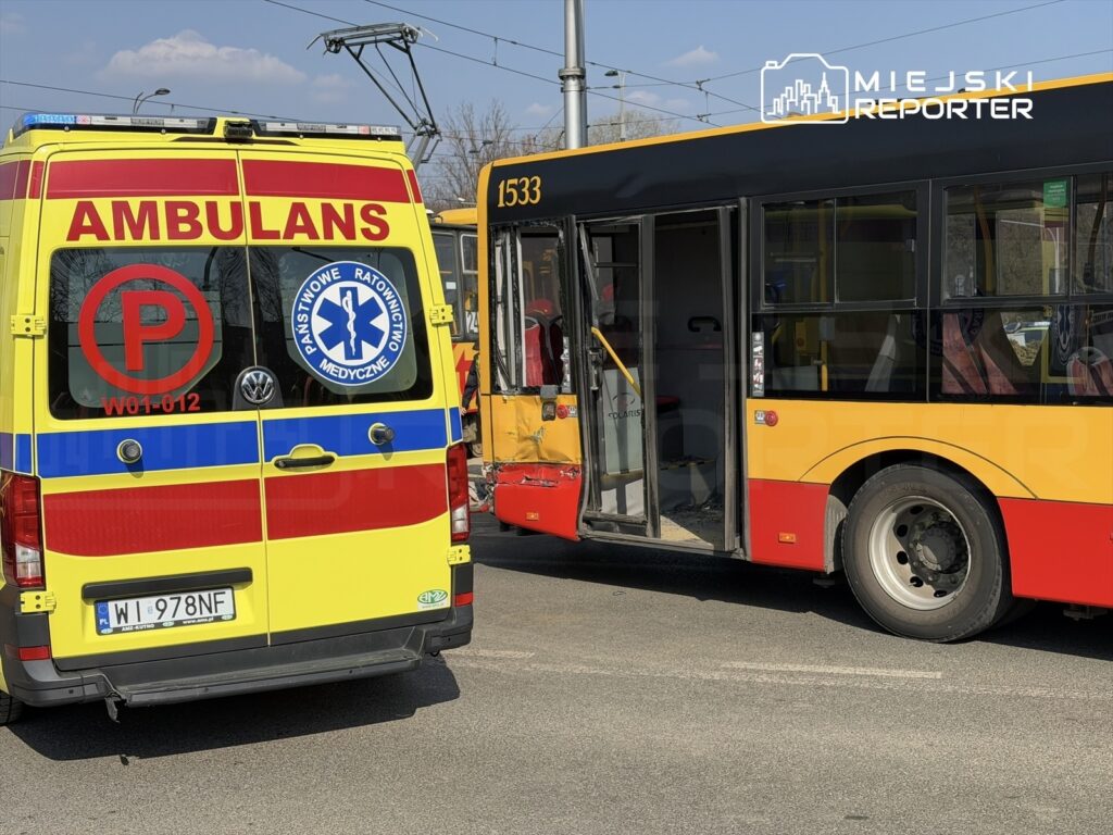 Karetka pogotowia z widocznym napisem "AMBULANS" stoi obok uszkodzonego autobusu miejskiego na jezdni.