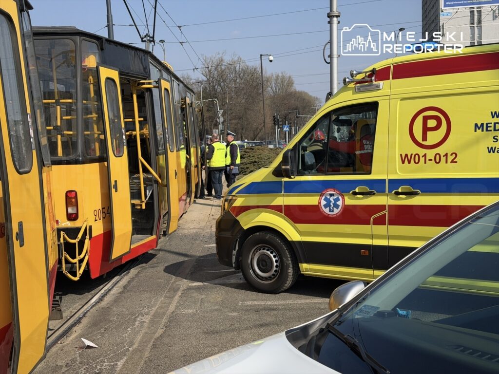 Tramwaj z otwartymi drzwiami zatrzymany obok karetki pogotowia, a obok grupka osób w kamizelkach odblaskowych.