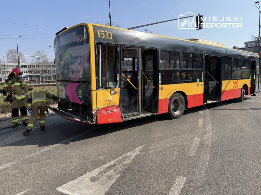 Strażacy badają uszkodzony autobus przystankowy na ulicy, obok otwartych drzwi pojazdu.