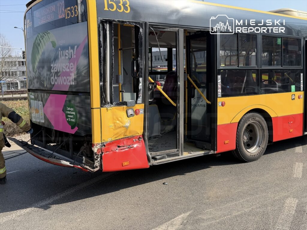 Wozidło komunikacji miejskiej z uszkodzeniem tyłu stoi na drodze, a strażak sprawdza sytuację.