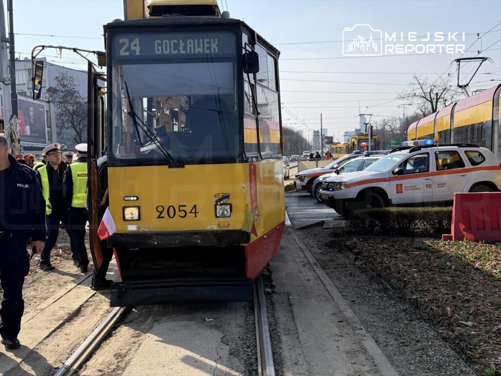 Tramwaj linii 24 stoi na torowisku, obok grupy policjantów i ratowników, w tle widać pojazdy służbowe.