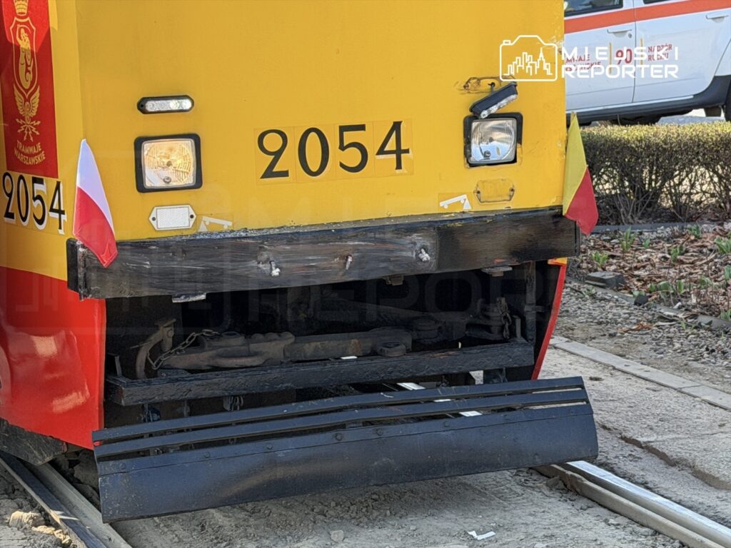 Żółty tramwaj z numerem 2054 stoi na torach, z widoczną flagą Polski i uszkodzoną przednią częścią.