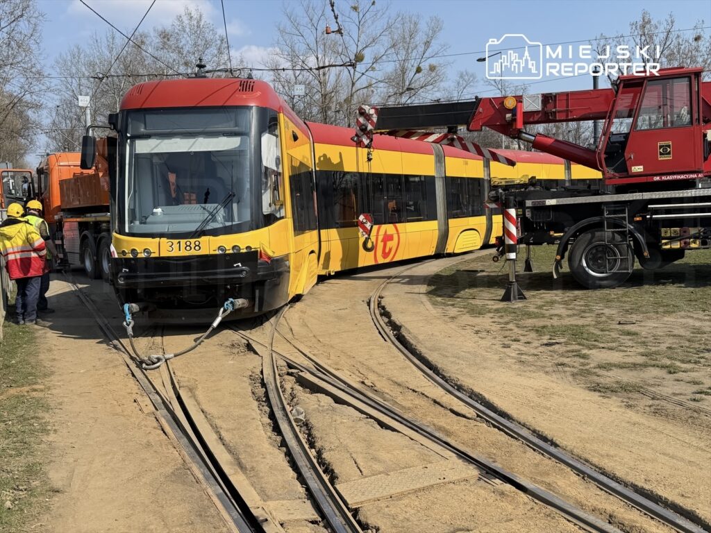 Tramwaj o numerze 3188 utknął na torach, a pracownicy w odblaskowych kamizelkach próbują go odciągnąć za pomocą dźwigu.