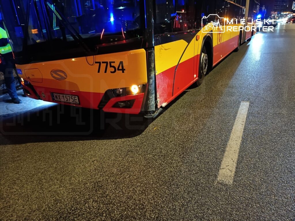 Autobus komunikacji miejskiej z numerem bocznym 7754 zatrzymany na ulicy, obok stojących funkcjonariuszy policji.