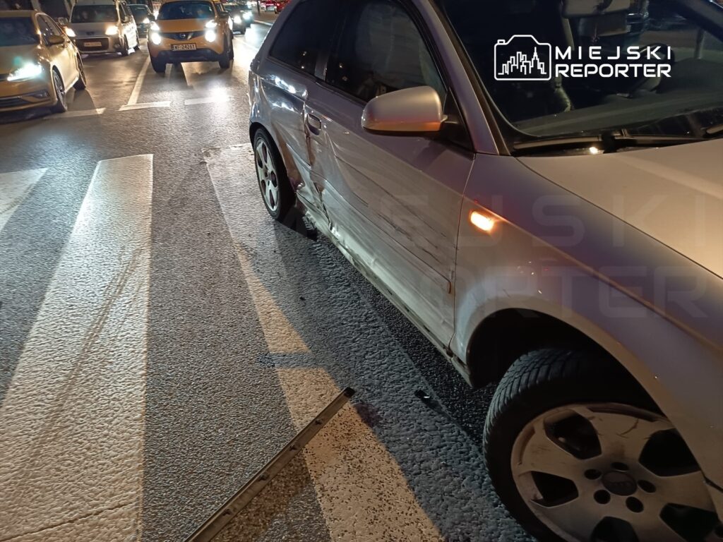 Uszkodzony samochód osobowy z wgniecioną karoserią stoi na pasach w ruchliwym mieście.
