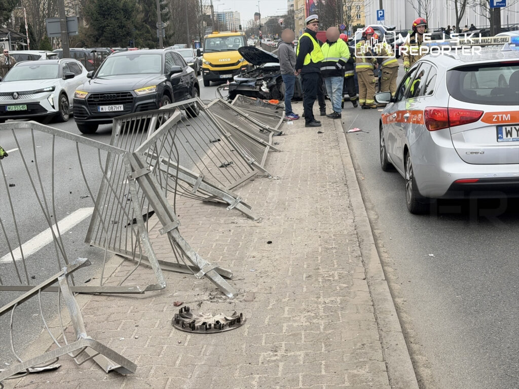 Grupa ratowników oraz policjantów udziela pomocy poszkodowanym po wypadku drogowym obok uszkodzonego samochodu.