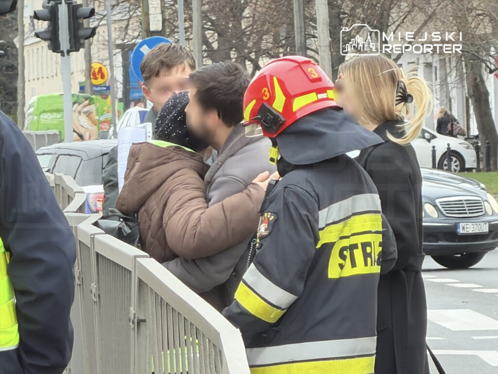 Grupa osób rozmawia na ulicy, a obok nich stoi strażak w mundurze.