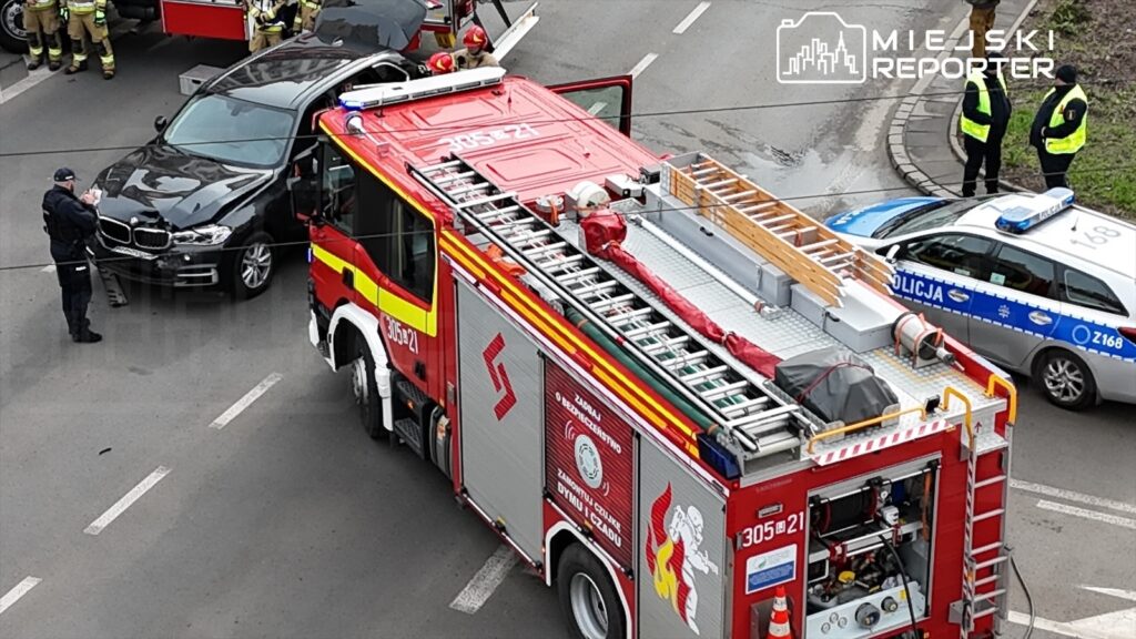 Strażacy oraz policjanci pracują przy wypadku drogowym, obok uszkodzonego samochodu osobowego i wozu strażackiego.