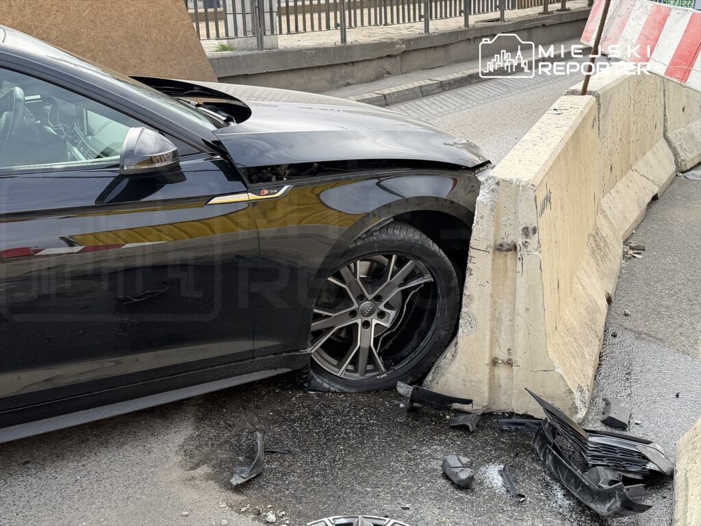 Czarny samochód osobowy uderzył w betonową barierę drogową, uszkadzając przednią część pojazdu.
