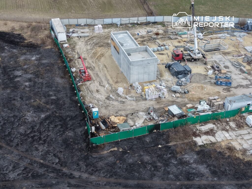 Budowa nowego obiektu w otoczeniu zniszczonej przez pożar ziemi, z widocznymi maszynami budowlanymi i materiałami.