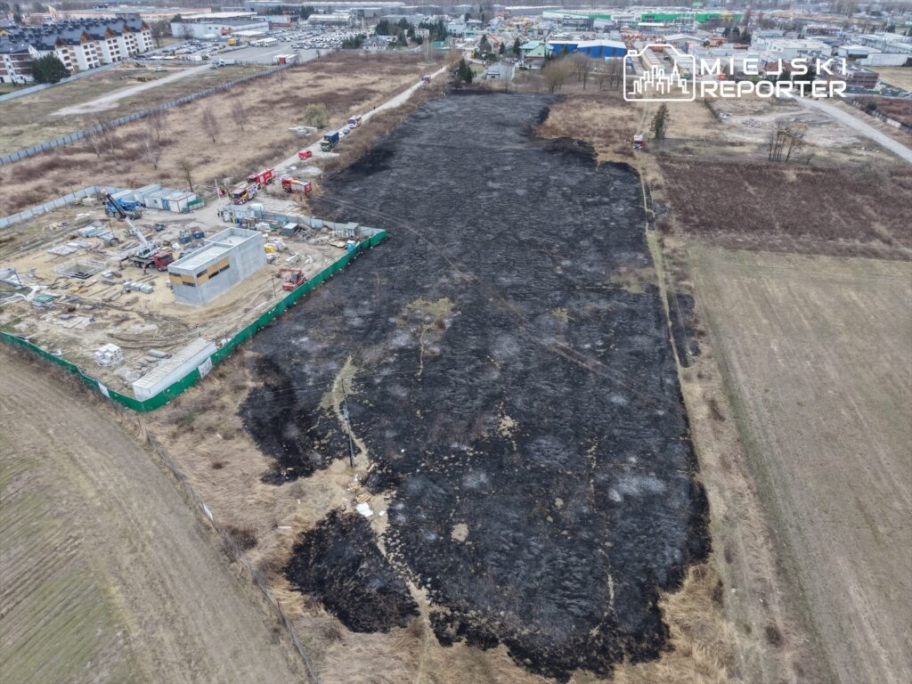 Na zniszczonym terenie widoczne są ślady po pożarze, a w tle trwa budowa nowego obiektu.