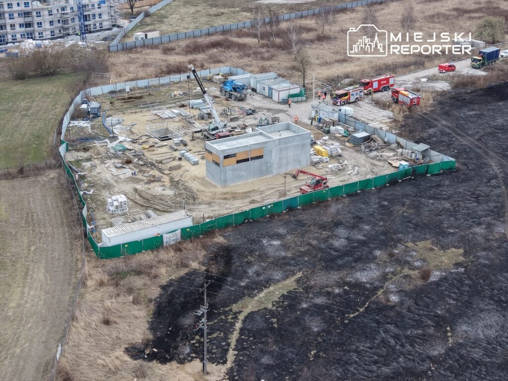 Budowa nowego obiektu z betonową konstrukcją oraz sprzętem budowlanym na placu w otoczeniu zarośniętej działki.