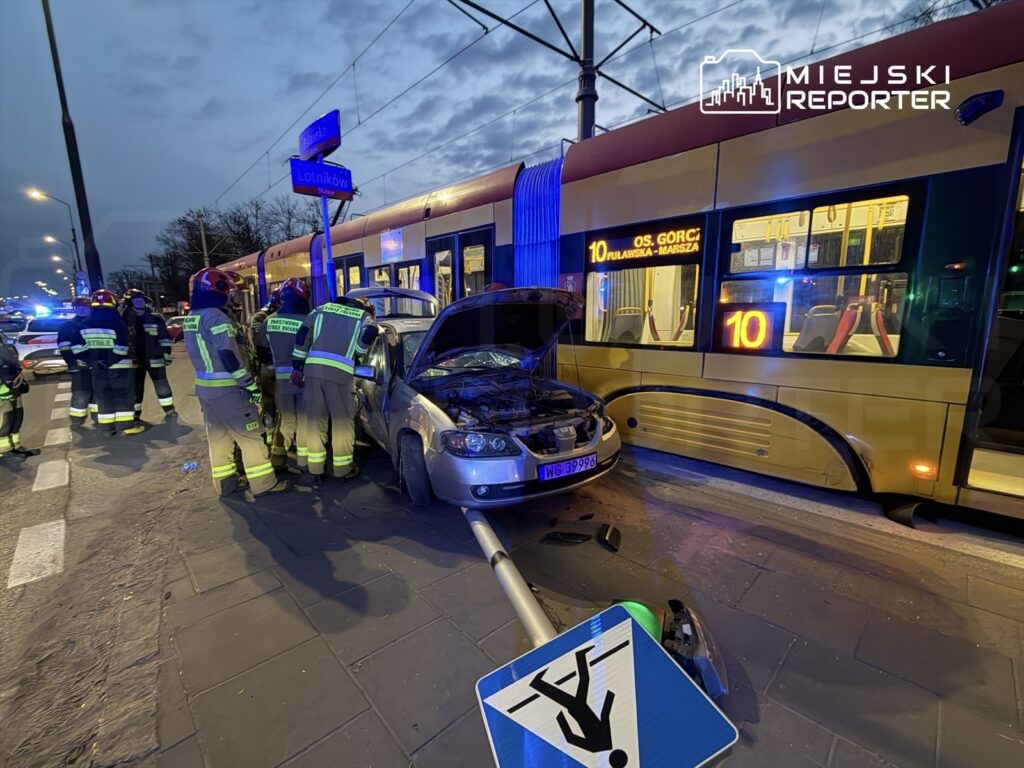 Grupa strażaków pracuje nad usunięciem uszkodzonego samochodu, który zderzył się z tramwajem na ruchliwej ulicy.