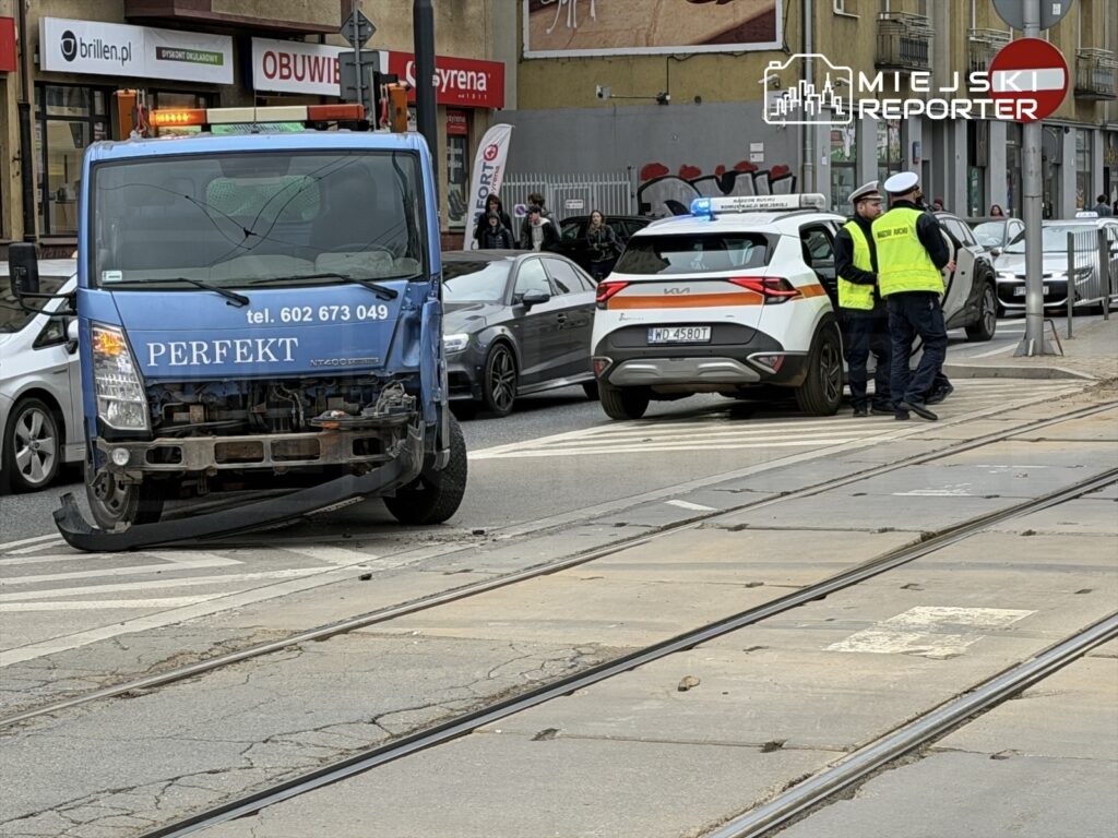 Niebieski pojazd z uszkodzonym przodem stoi na torowisku, obok interweniujący policjanci rozmawiają z kierowcą.