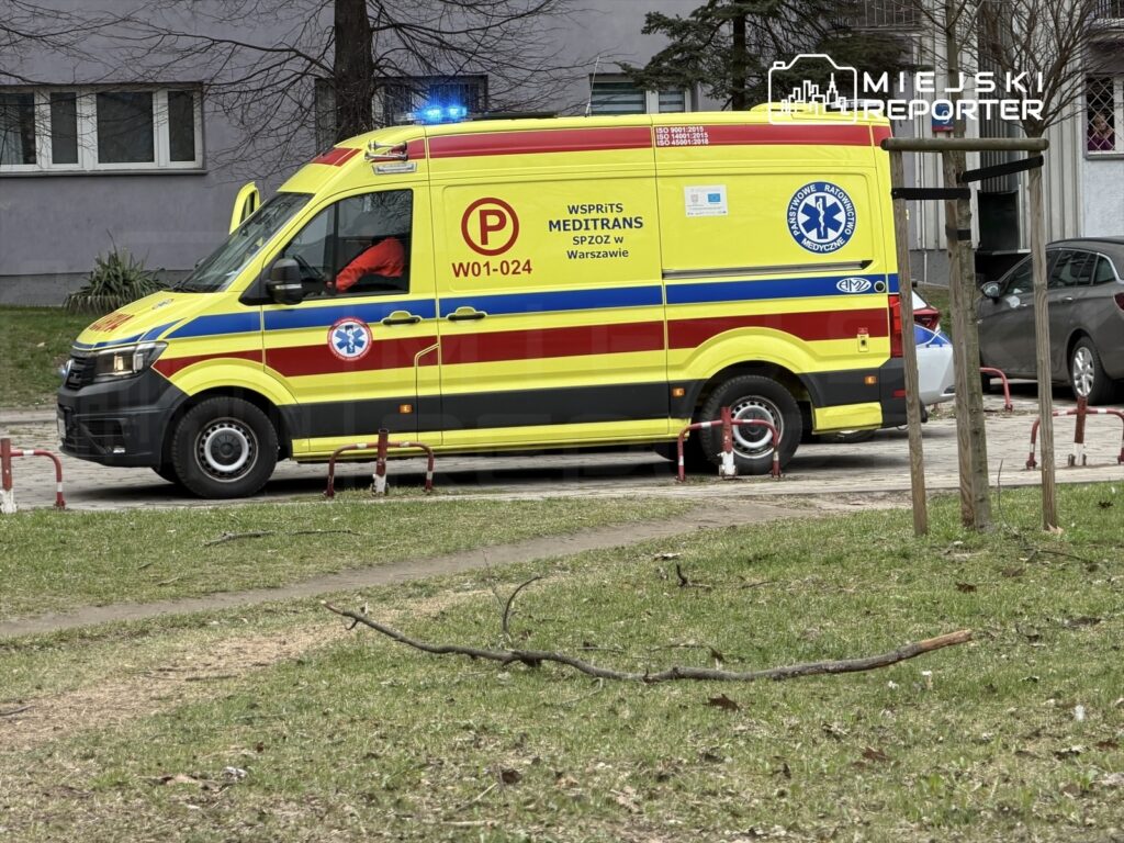 Karetka pogotowia w żółto-czerwonych barwach zaparkowana na chodniku obok budynku mieszkalnego.