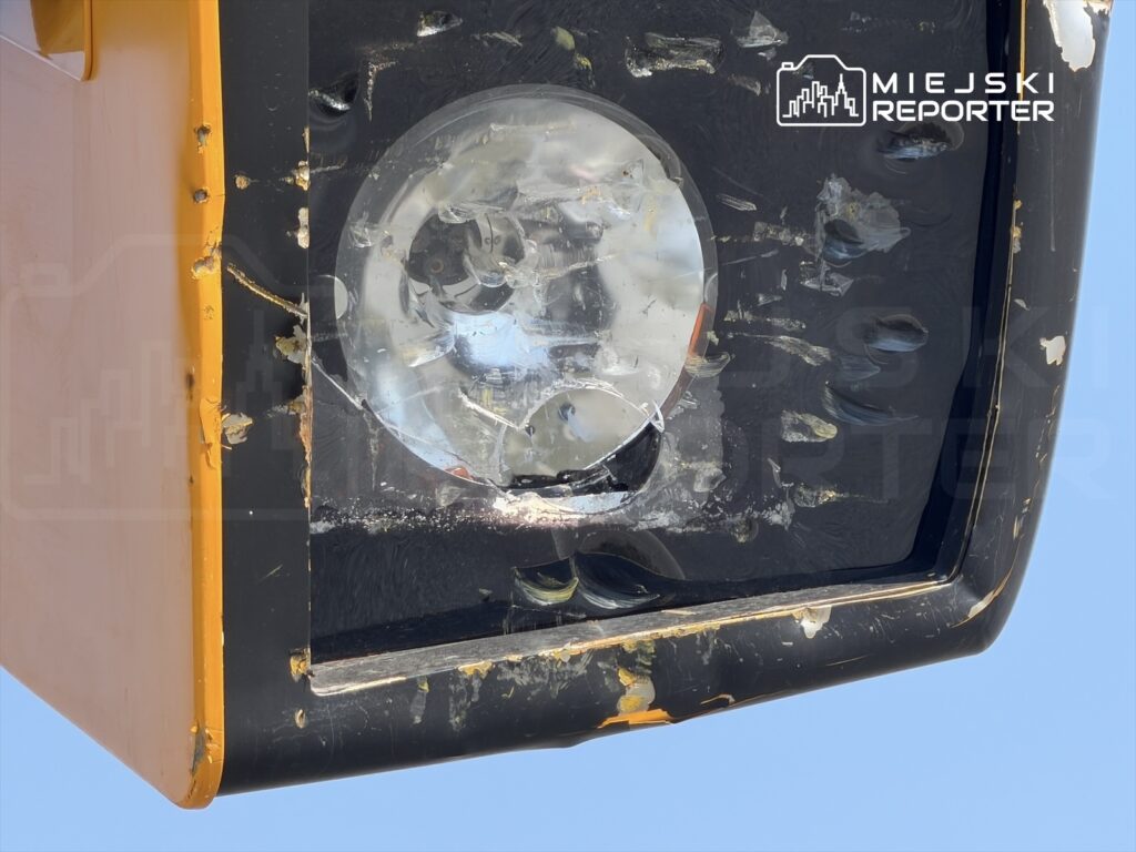 Uszkodzone światło sygnalizacyjne z widocznymi rysami oraz odpryskami farby na czarnej obudowie.