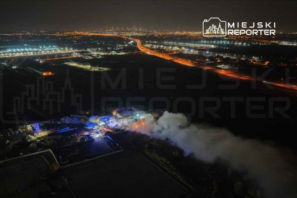 Akcja ratunkowa z użyciem wozów strażackich w nocy, w tle widoczne oświetlone miasto.