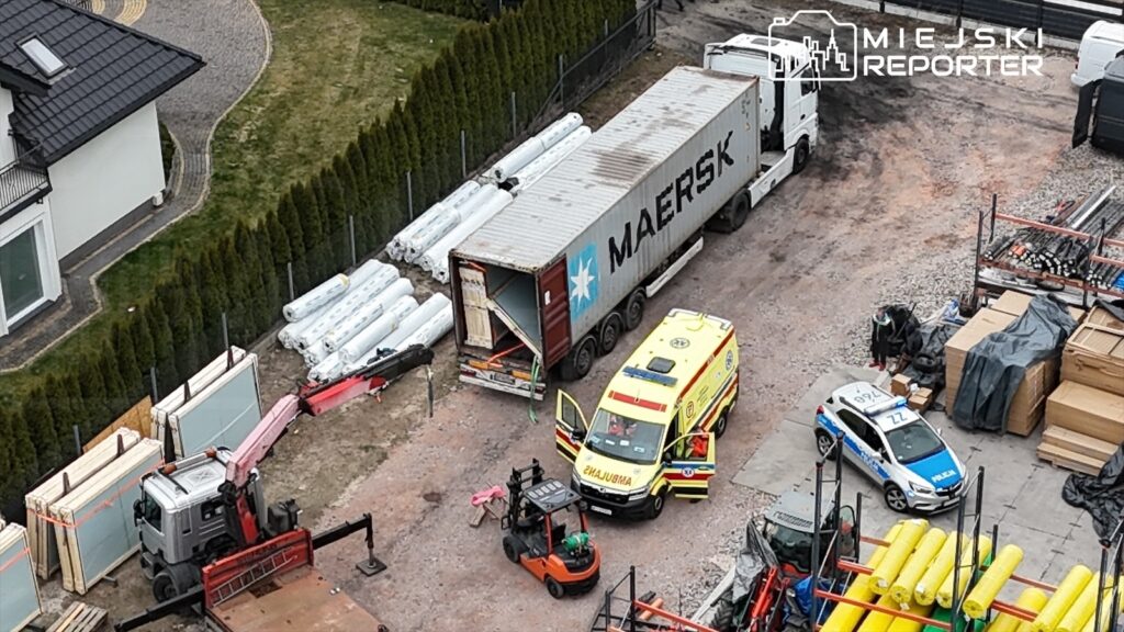 Na placu budowy parkowany jest ciężarowy kontener, obok stoi karetka pogotowia i radiowóz policyjny.