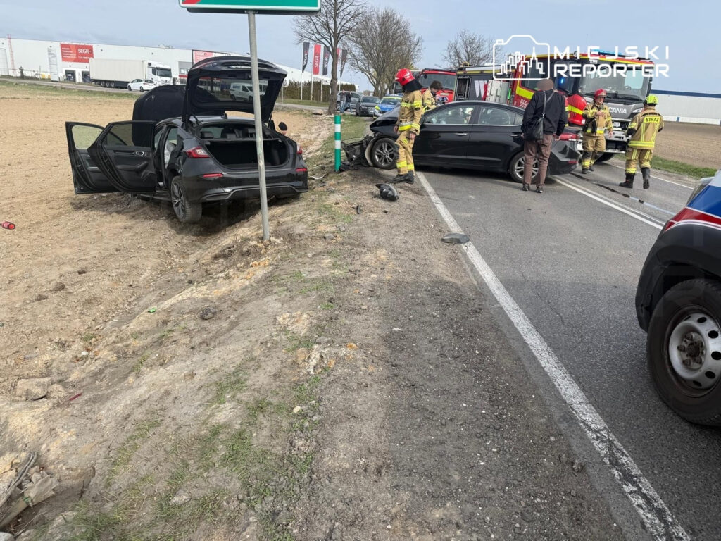 W miejscu wypadku drogowego, strażacy udzielają pomocy poszkodowanym przy uszkodzonych pojazdach.