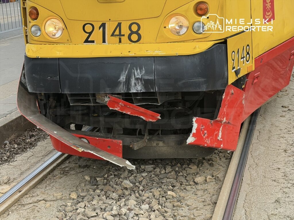 Zniszczony przód tramwaju z numerem 2148, z uszkodzoną czerwoną osłoną, stojącego na torach w miejskim otoczeniu.