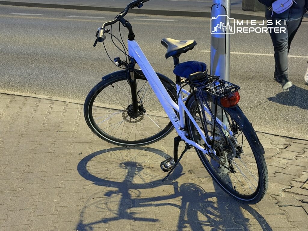 Rower stojący na chodniku, z widocznymi cieniami, obok latarni ulicznej.