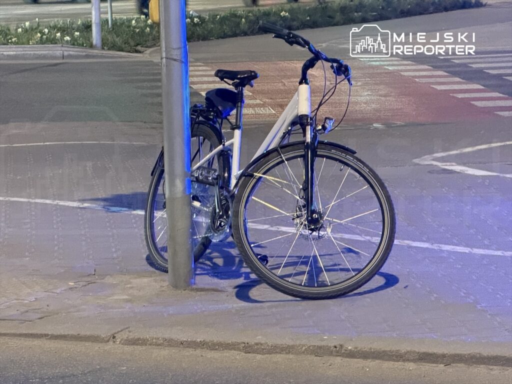 Rower przyparty do słupa na oświetlonej ulicy, w tle widoczne światła samochodów.