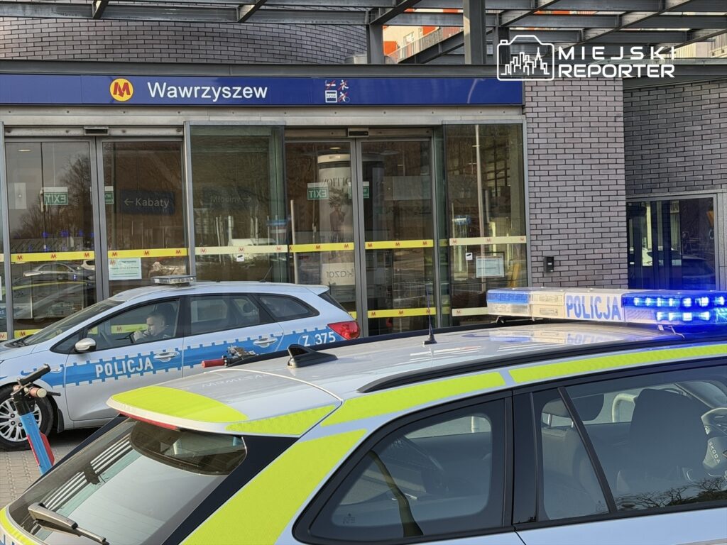 Policyjny radiowóz z włączonymi sygnałami świetlnymi zaparkowany przed stacją metra Wawrzyszew.