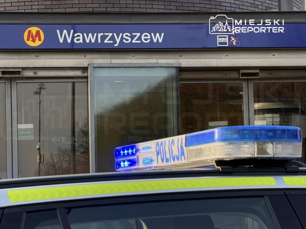Policyjny radiowóz z włączonymi sygnałami świetlnymi przed wejściem na stację metra Wawrzyszew.