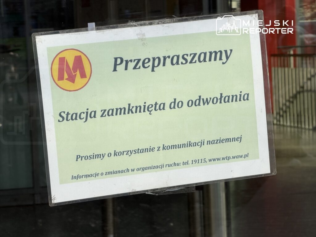 Zielony plakat informacyjny z napisem "Przepraszamy, Stacja zamknięta do odwołania" umieszczony w drzwiach stacji metra.