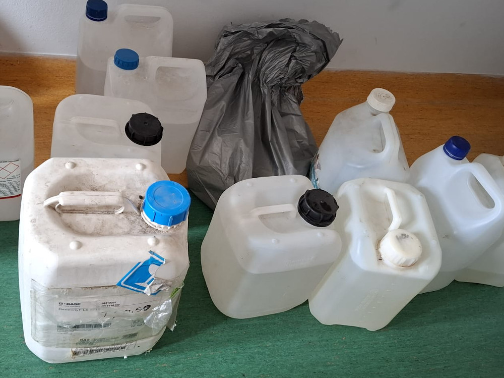 Grupa plastikowych pojemników o różnych rozmiarach i kolorach nakrętek, leżących na zielonym podłożu obok szarego worka.