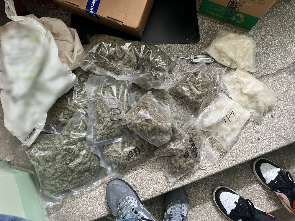 Zestawienie kilku przezroczystych torebek z suszem roślinnym oraz białym proszkiem leżących na posadzce. W tle widoczny karton.