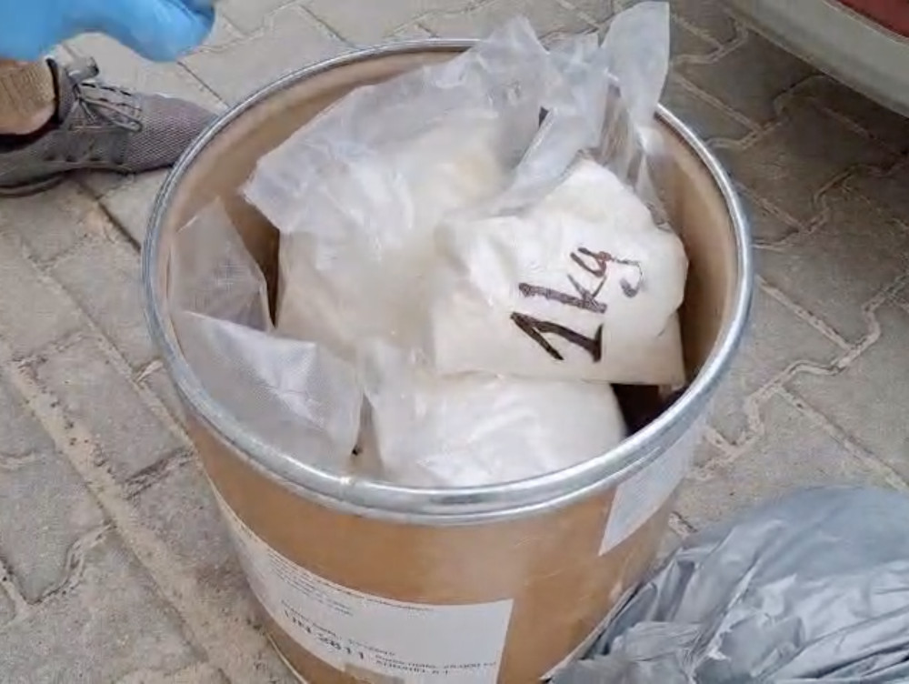 Mężczyzna w rękawiczkach dotyka pojemnika z pakietami białego proszku, oznaczonymi jako 1 kg.