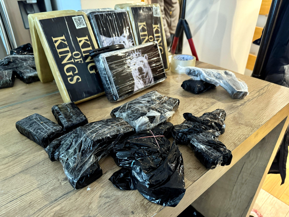 Na stole leżą opakowane przedmioty, w tym pistolety i pakunki, obok książki z napisem "KING OF KINGS".