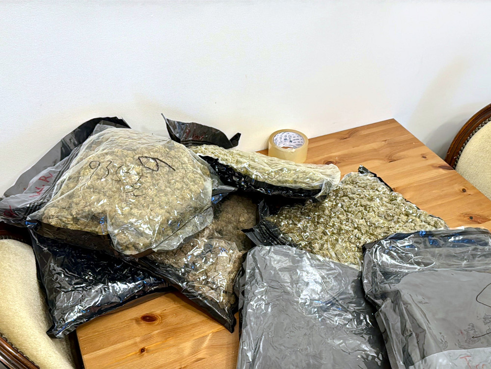 Pakiety zielonego materiału w przezroczystych torebkach leżą na drewnianym stole obok rolki taśmy.