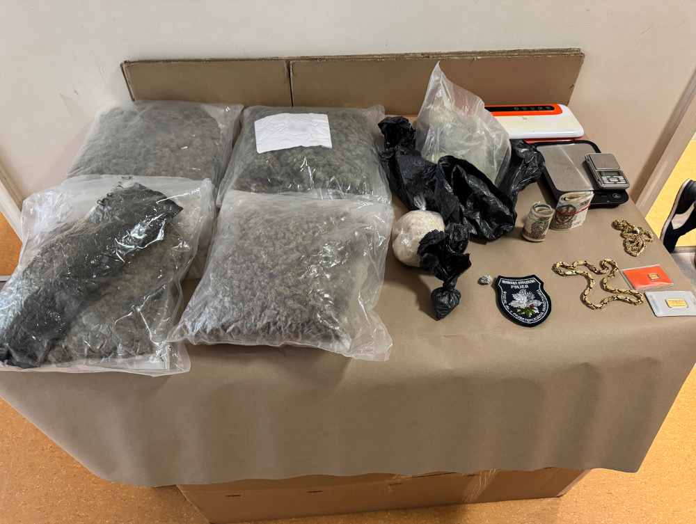 Na stole znajdują się zapakowane worki z suszem, waga, nieoznakowane przedmioty oraz emblemat policyjny.