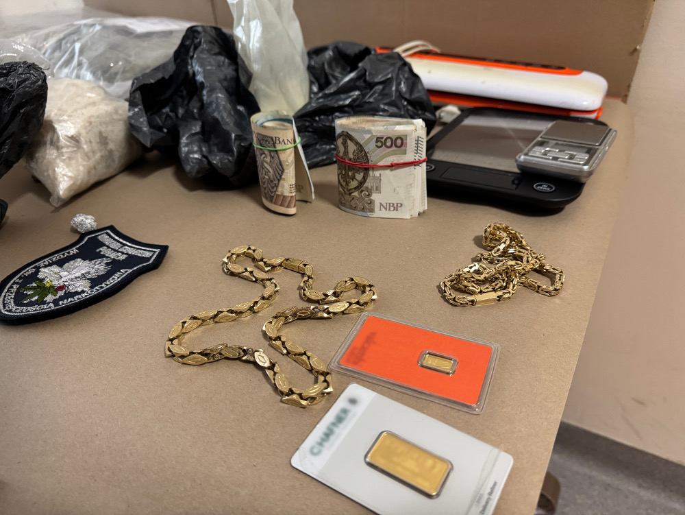 Na stole leżą różne przedmioty, w tym złote biżuterie, banknoty 500 zł, oraz waga elektroniczna.