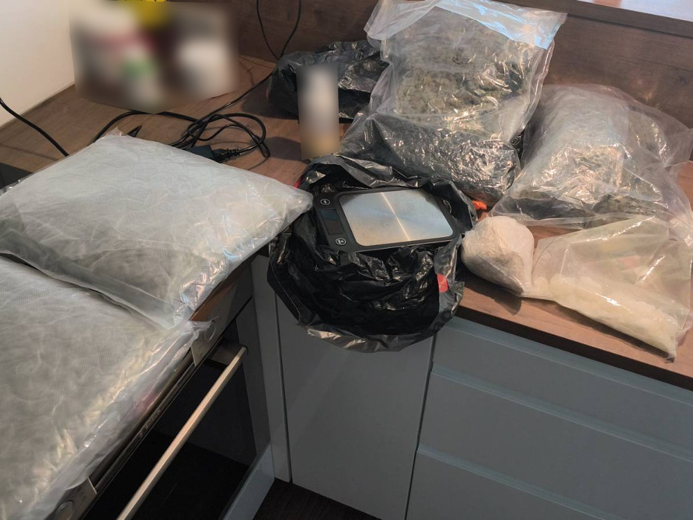 Na blacie kuchennym znajdują się różne pakunki z substancjami, w tym woreczki oraz waga elektroniczna.