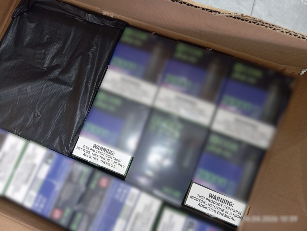 Czarny pakunek leżący w pudełku z widocznymi ostrzeżeniami o zawartości nikotyny na opakowaniach.