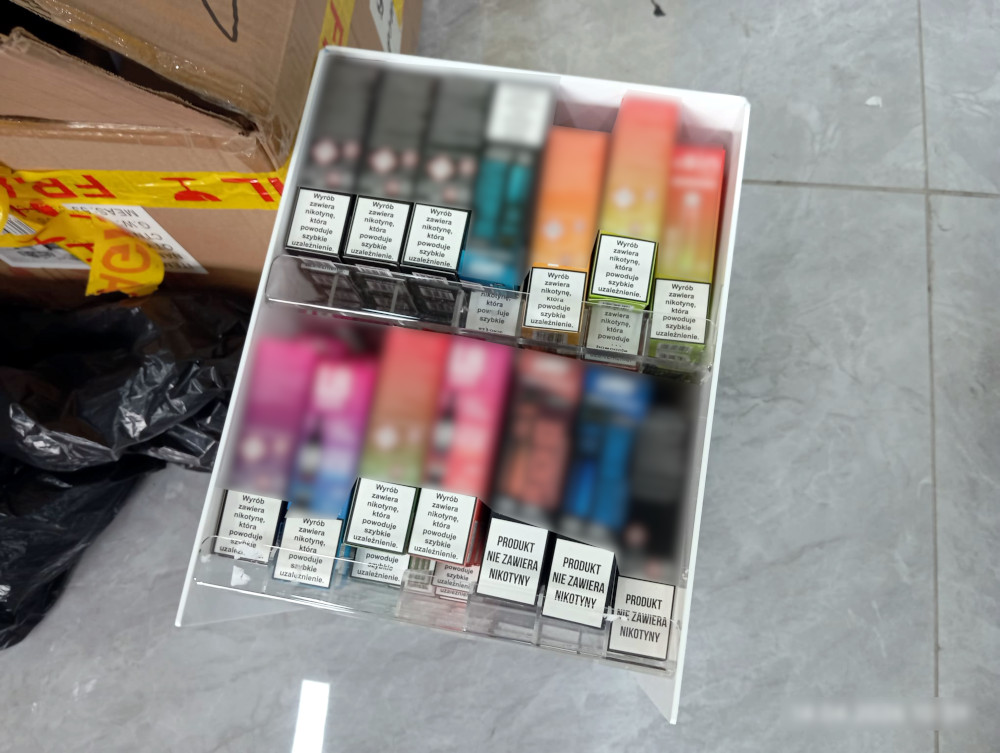 Półka z różnokolorowymi opakowaniami e-papierosów, niektóre z napisami ostrzegawczymi o zawartości nikotyny.