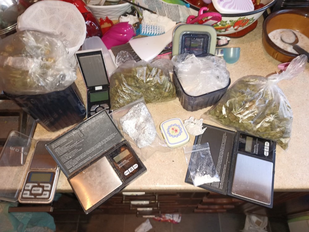 Na blacie kuchennym znajdują się wagi elektroniczne oraz kilka torebek z suszem roślinnym, w tym jedna w przezroczystej folii.